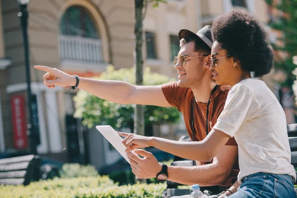 Jovem viajante do sexo masculino apontando por dedo para afro-americana namorada com tablet digital — Fotografia de Stock