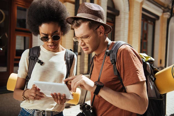 Seria pareja multicultural de turistas con tableta digital en busca de destino - foto de stock