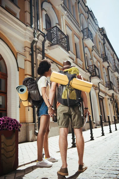 Vista posteriore di coppia di turisti con stuoie, zaini e tablet digitale — Foto stock