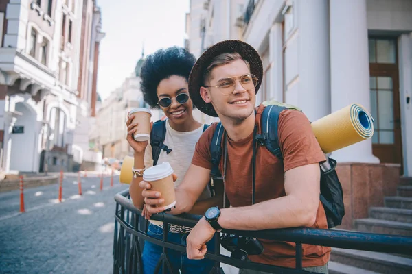 Sorridente coppia multiculturale di turisti in piedi con tazze di caffè usa e getta — Foto stock