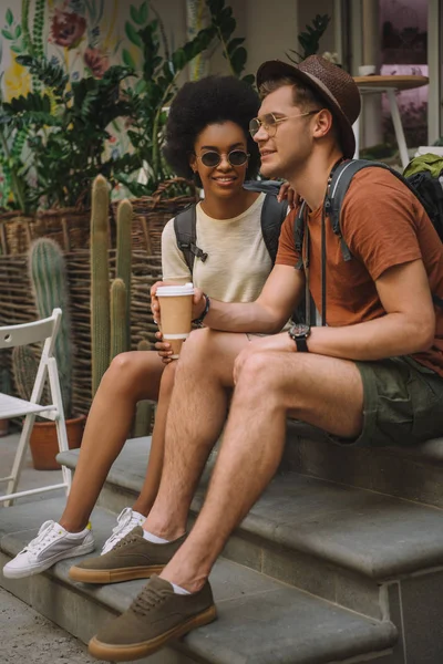 Joven pareja multicultural con café sentado en las escaleras - foto de stock