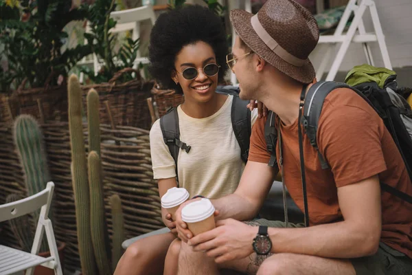 Elegante casal interracial sentado com copos de papel de café — Fotografia de Stock