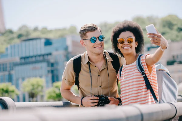 Jovem casal multicultural de viajantes levando selfie no smartphone — Fotografia de Stock