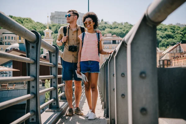 Міжрасові пари молодих мандрівників з камерою та рюкзаки, ходьба на мосту — стокове фото