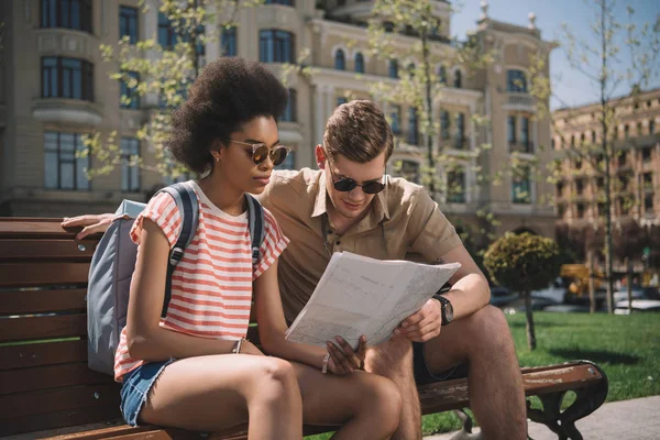 Couple of young tourists looking at map on bench — Stock Photo