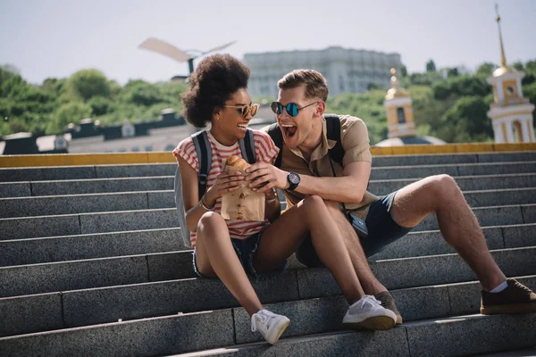 Junger männlicher Reisender versucht Freundin Croissant auf Treppe zu essen — Stockfoto