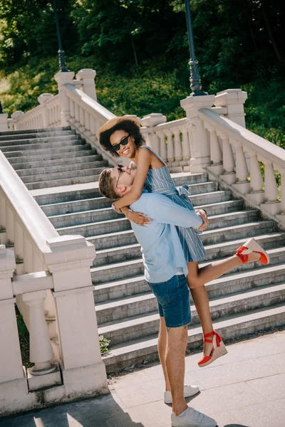 Joven sosteniendo sonriente novia cerca de escaleras parque - foto de stock