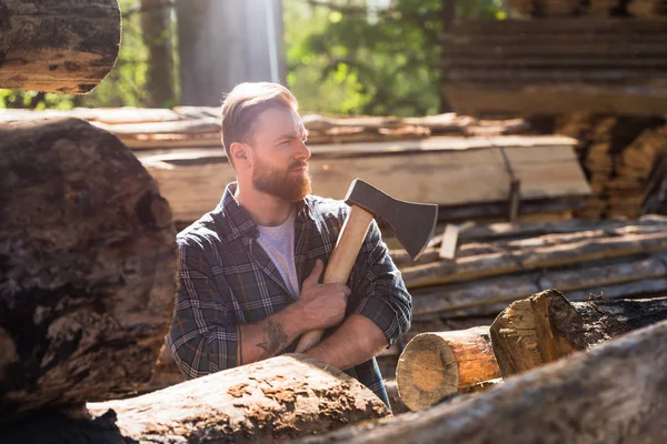 Side view of lumberjack in checkered shirt with tattooed hand holding axe at sawmill — Stock Photo