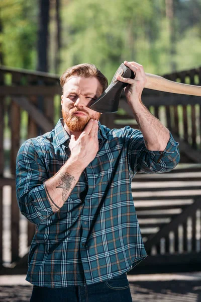 Bärtiger Holzfäller mit tätowierter Handrasur per Axt im Sägewerk — Stockfoto