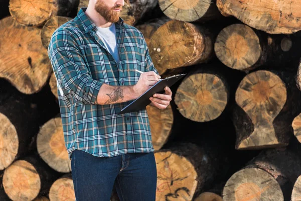 Zugeschnittenes Bild eines Holzfällers in kariertem Hemd, Schrift in Klemmbrett auf Protokollhintergrund — Stockfoto