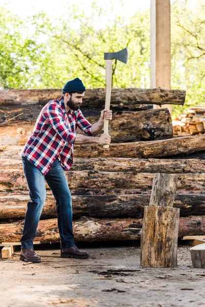 Bearded lumberjack in checkered shirt chopping log at sawmill — Stock Photo