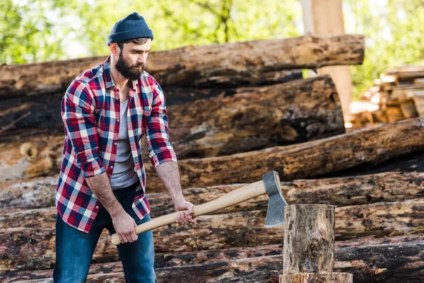 Bearded lumberjack in checkered shirt chopping log at sawmill — Stock Photo