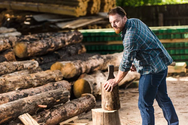 Bärtiger Holzfäller im karierten Hemd hackt Baumstamm im Sägewerk — Stockfoto