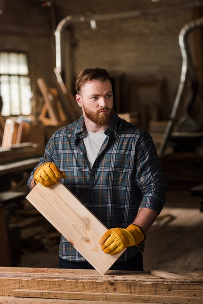 Tischler in Schutzhandschuhen arbeitet im Sägewerk mit Holzplanke — Stockfoto