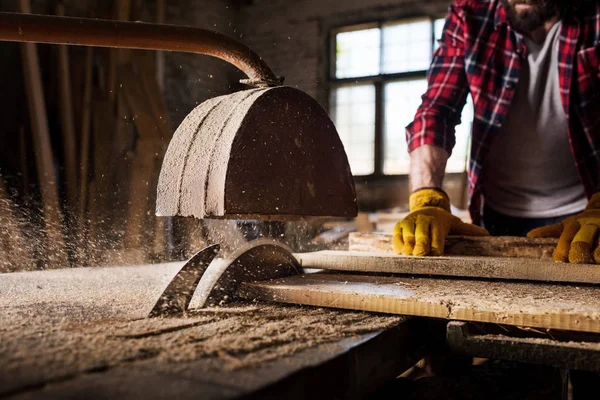 Cropped image of carpenter in protective gloves  using machine saw at sawmill — Stock Photo