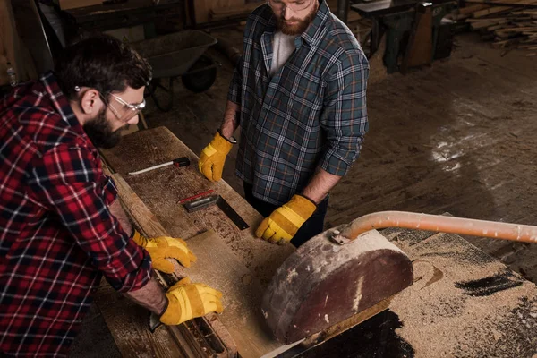 Vue grand angle de deux charpentiers utilisant une scie mécanique à la scierie — Photo de stock