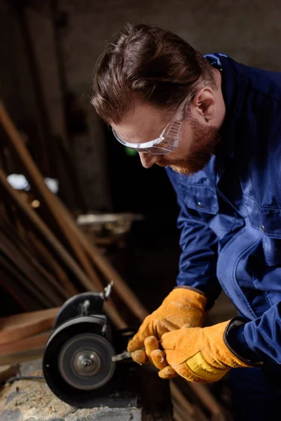 Trabajador en googles y guantes protectores utilizando la máquina de pulir en el aserradero - foto de stock