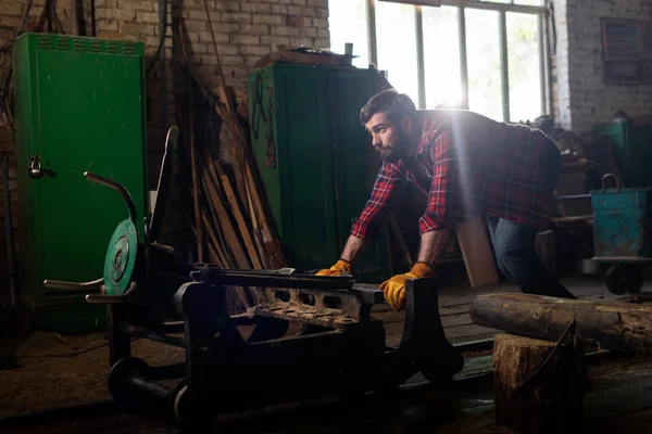 Vue latérale du travailleur dans des gants de protection poussant la machine à la scierie — Photo de stock