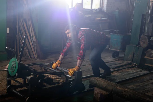 Trabalhador barbudo em luvas de proteção empurrando máquina na serraria — Fotografia de Stock