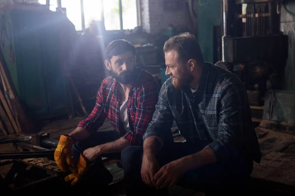 Dos trabajadores barbudos sentados y hablando entre sí en el aserradero - foto de stock