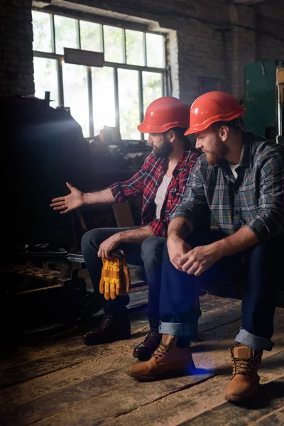 Worker in protective helmet pointing on machine to colleague at sawmill — Stock Photo