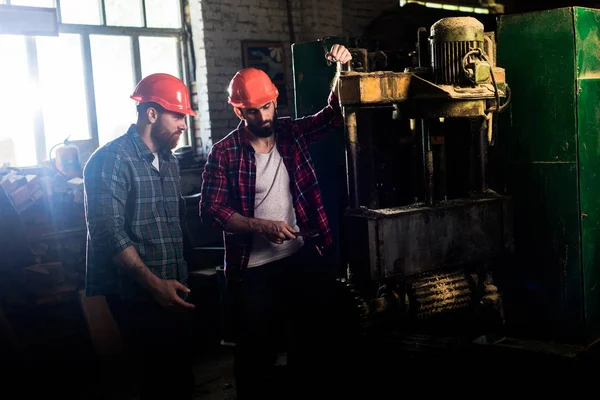 Carpenters in protective helmets using machine tool at sawmill — Stock Photo