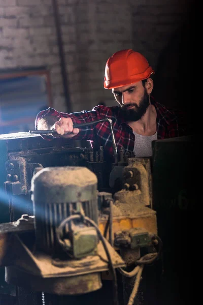 Worker in protective helmet repairing machine tool at sawmill — Stock Photo