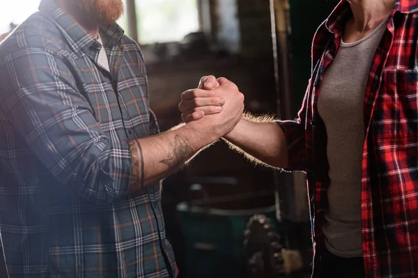 Immagine ritagliata di falegname con mano tatuata che stringe la mano del partner in segheria — Foto stock