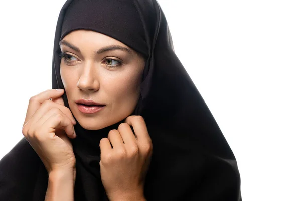 Hermosa joven musulmana en hiyab con las manos cerca de la cara mirando hacia otro lado aislado en blanco - foto de stock