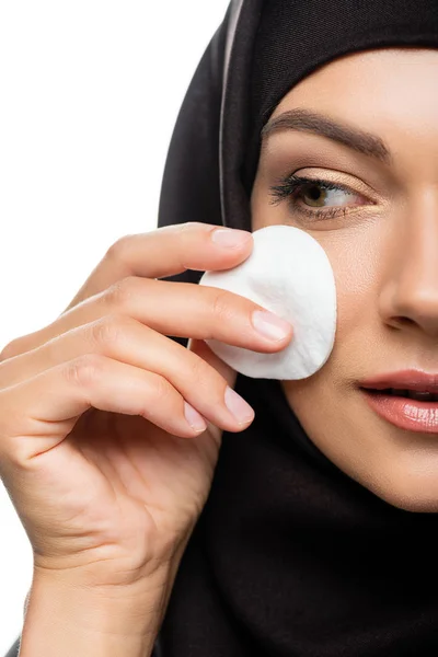 Vue recadrée de la jeune femme musulmane en hijab essuyant visage avec tampon de coton isolé sur blanc — Photo de stock