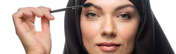 Young Muslim woman in hijab applying mascara on eyelashes isolated on white, panoramic shot — Stock Photo