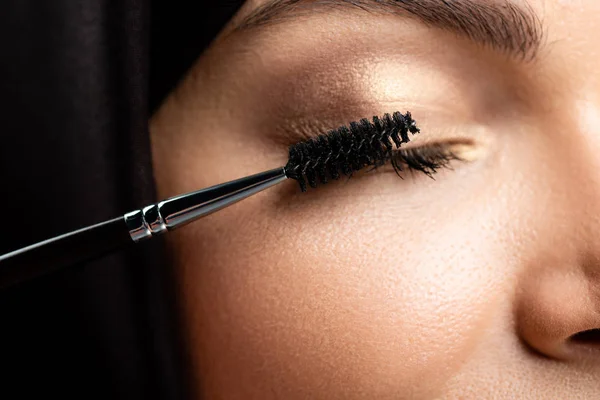 Close up view of young Muslim woman in hijab applying mascara on eyelashes with closed eyes — Stock Photo