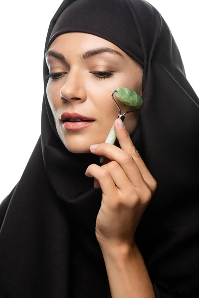 Joven musulmana en hijab usando rodillo de jade aislado en blanco - foto de stock