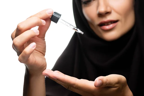 Enfoque selectivo de la joven musulmana en hijab sosteniendo gotero con suero aislado en blanco - foto de stock