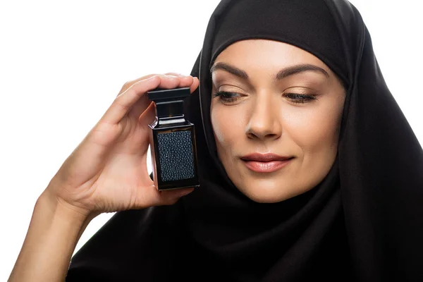 Молодая мусульманка в хиджабе смотрит на бутылку духов, изолированных на белом — стоковое фото