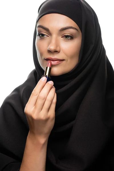 Jeune femme musulmane en hijab appliquant rouge à lèvres beige isolé sur blanc — Photo de stock