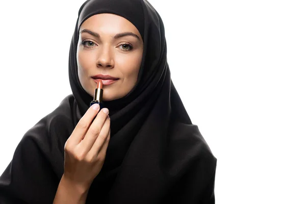 Joven musulmana en hijab aplicando lápiz labial beige aislado en blanco - foto de stock