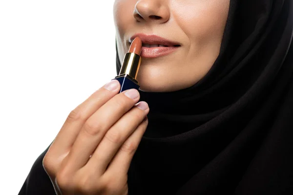 Vista recortada de la joven musulmana en hijab aplicando lápiz labial beige aislado en blanco - foto de stock