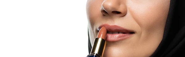 Cropped view of young Muslim woman in hijab applying beige lipstick isolated on white, panoramic shot — Stock Photo