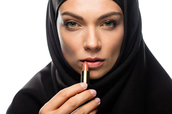 Joven musulmana en hijab aplicando lápiz labial beige aislado en blanco - foto de stock