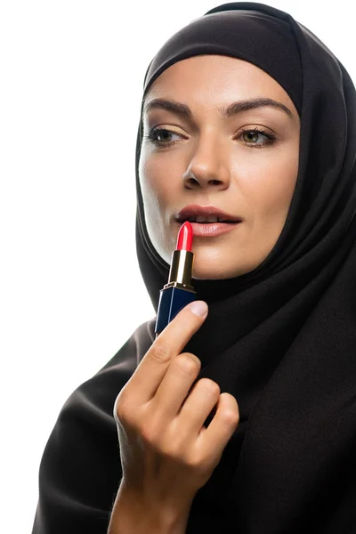 Joven musulmana en hiyab aplicando lápiz labial rojo aislado en blanco - foto de stock