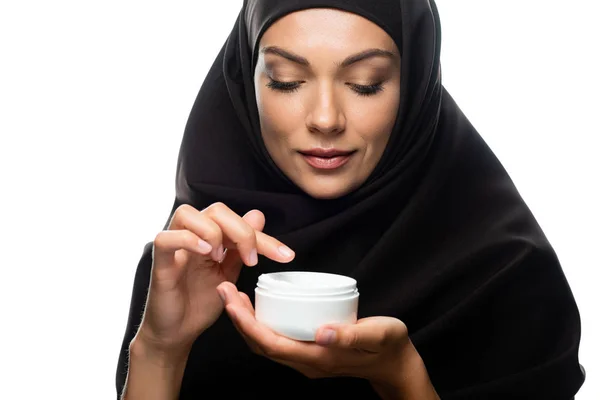 Young Muslim woman in hijab holding container with cosmetic cream isolated on white — Stock Photo