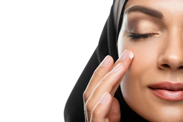 Vue recadrée de la jeune femme musulmane dans le hijab appliquant crème faciale avec les yeux fermés isolé sur blanc — Photo de stock