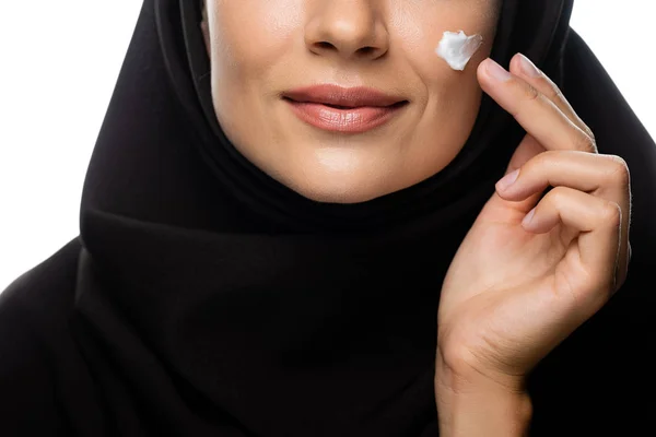 Vista recortada de la joven musulmana en hiyab aplicando crema cosmética en el polluelo aislado en blanco - foto de stock