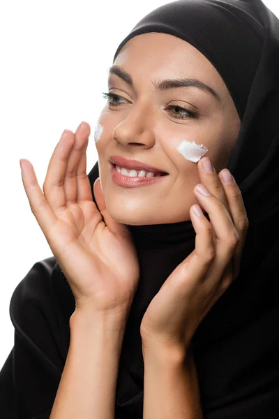 Heureuse jeune femme musulmane en hijab appliquer la crème cosmétique sur les poussins isolés sur blanc — Photo de stock