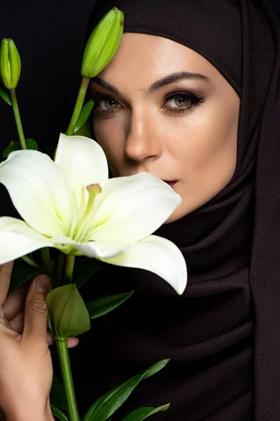 Beautiful Muslim woman in hijab with smoky eyes holding lily isolated on black — Stock Photo