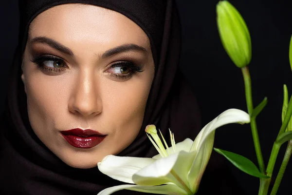 Jolie femme musulmane en hijab avec des lèvres rouges près de lis isolé sur noir — Photo de stock