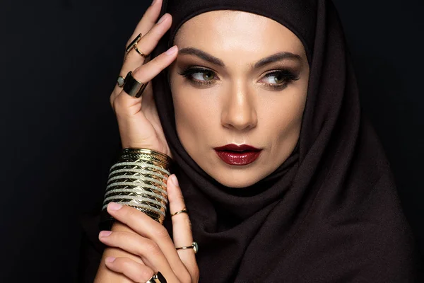 Beautiful Muslim woman in hijab with makeup in golden rings and bracelet isolated on black — Stock Photo