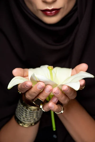 Beautiful Muslim woman in hijab in golden rings and bracelet holding lily isolated on black — Stock Photo
