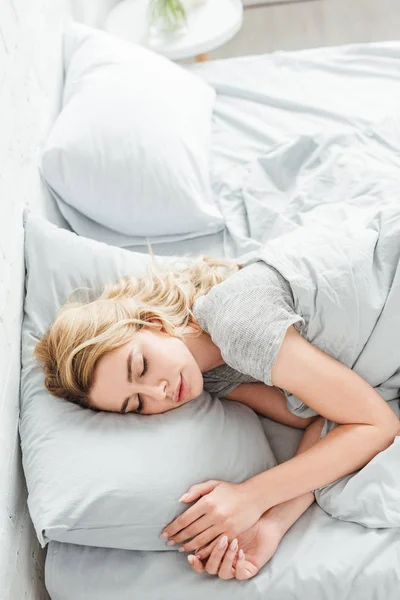 Vista aérea de la hermosa mujer joven durmiendo debajo de la manta en casa - foto de stock